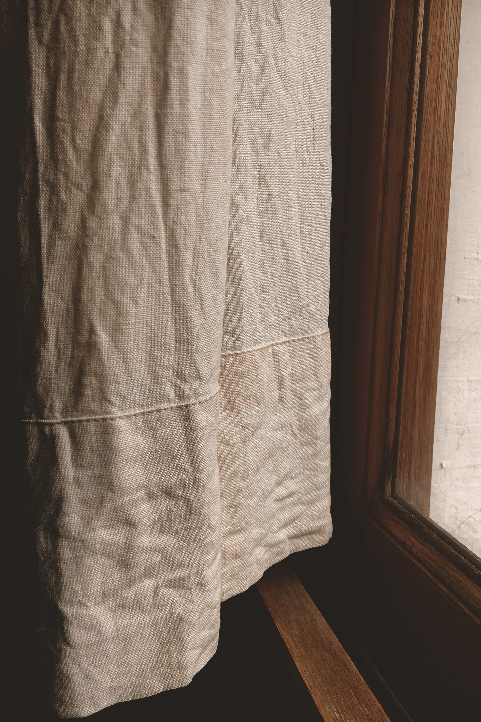 A linen curtain hanging beside a wooden window frame in natural light